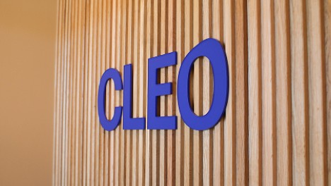 Blue 'CLEO' logo on a wooden panel background