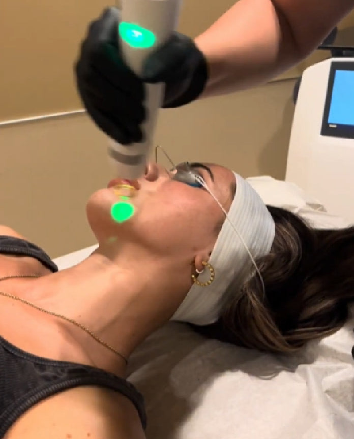 Person receiving a facial treatment with green lights and medical equipment.