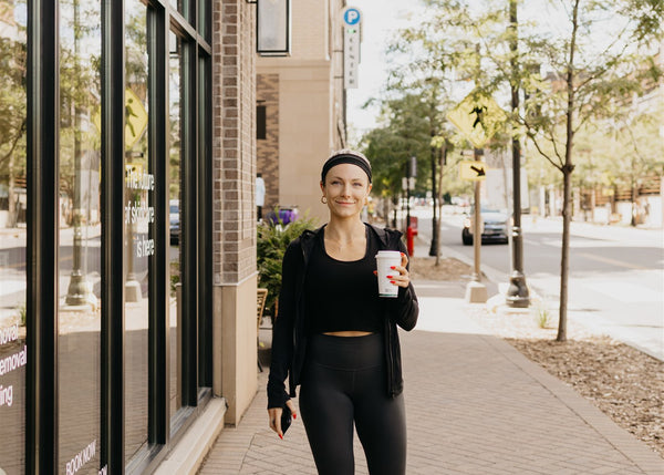 Woman walking with cup of coffee in front of Cleo Skin + Laser location