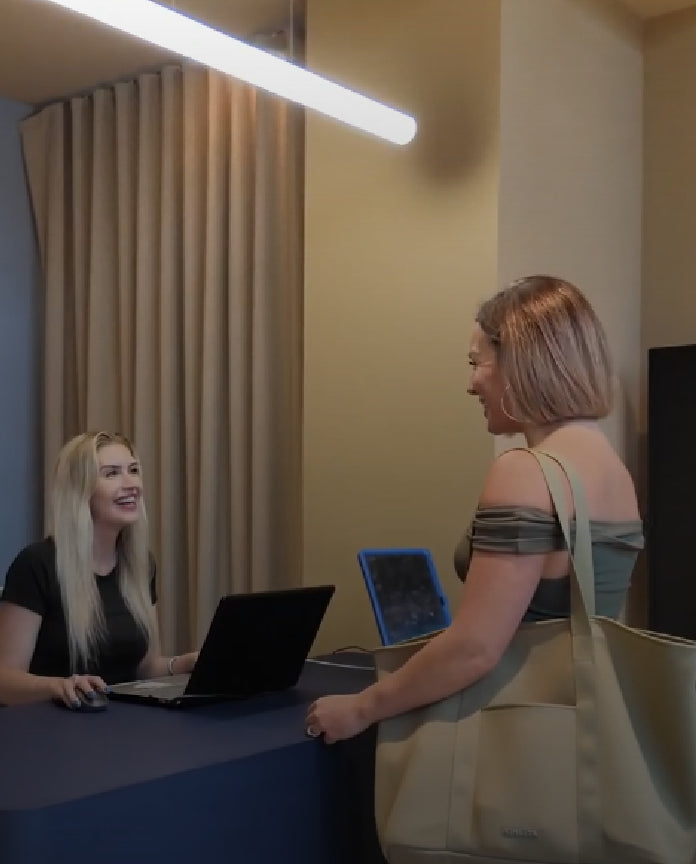 Two women at a desk with a laptop and tablet, one standing and the other sitting.