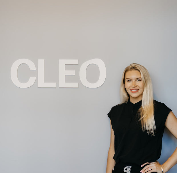 Smiling woman standing in front of grey wall with Cleo branding on it